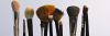 A variety of makeup brushes arranged vertically on a plain backdrop, perfect for beauty and cosmetic themes.